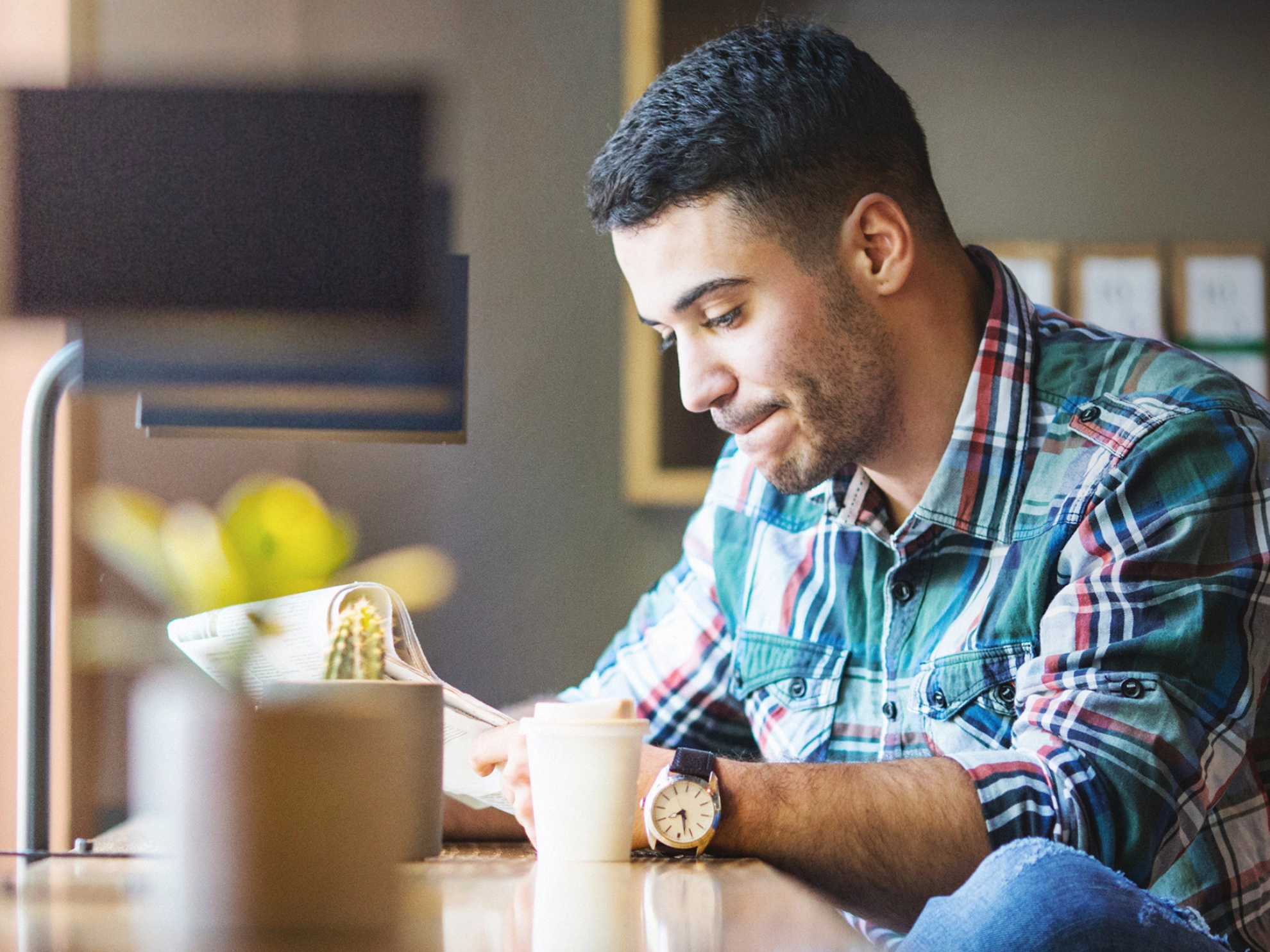 Ein junger Mann liest Zeitung und trinkt dabei Kaffee.